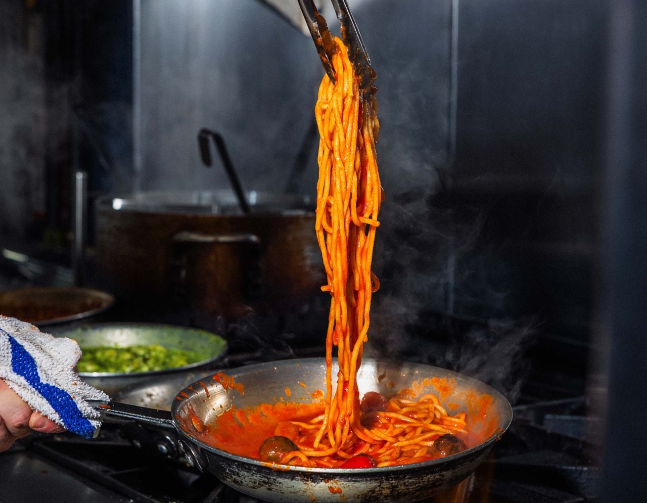A chef uses tongs to take spaghetti from a pan