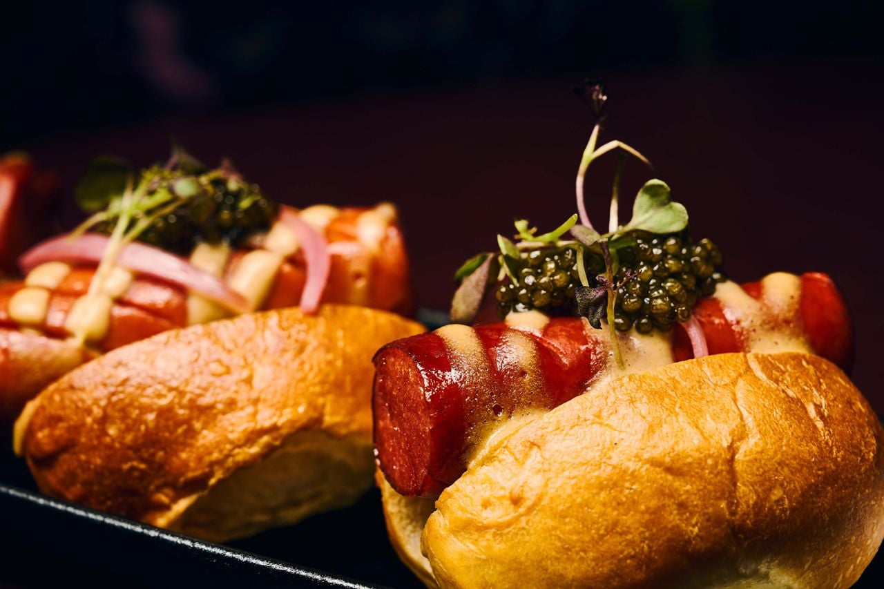 A closeup of a mini Wagyu hot dog topped with caviar