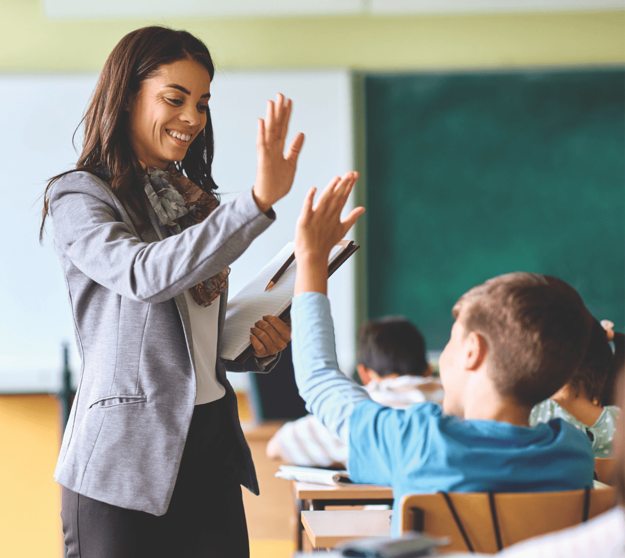 A teacher in a classroom high-fives a boy student.