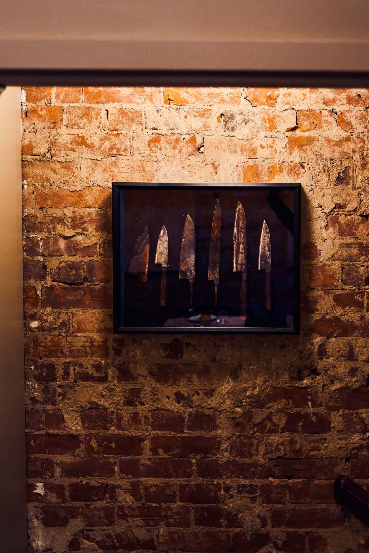 A selection of chefs knives, framed and hanging on a brick wall