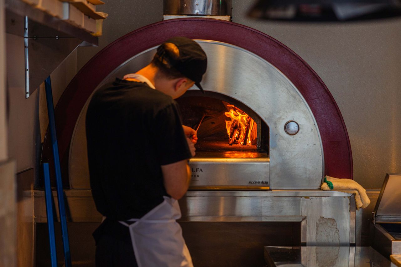 A chef pulls a pizza out of a wood-fired oven