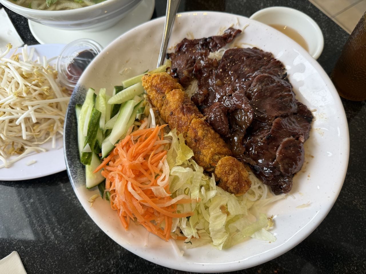 A plate of beef, noodles, a spring roll and veggies