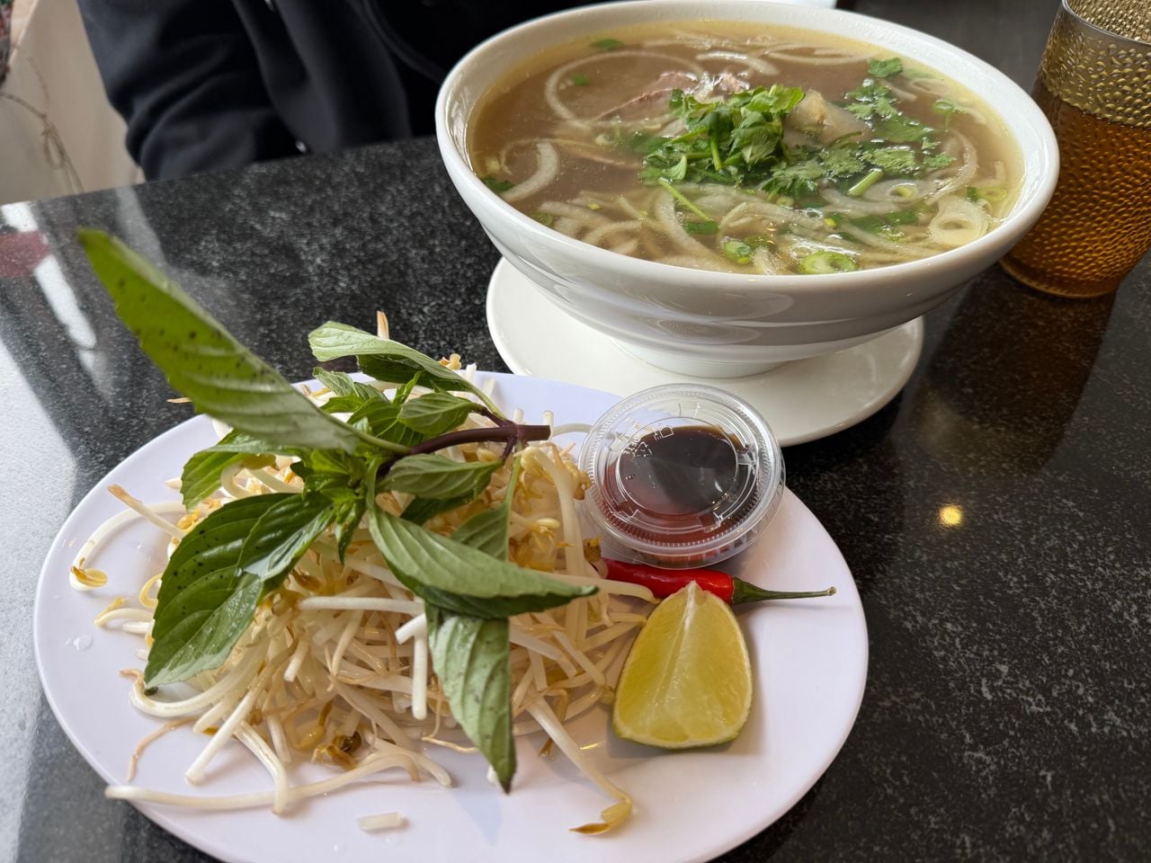 An order of pho with a plate of bean sprouts and basil