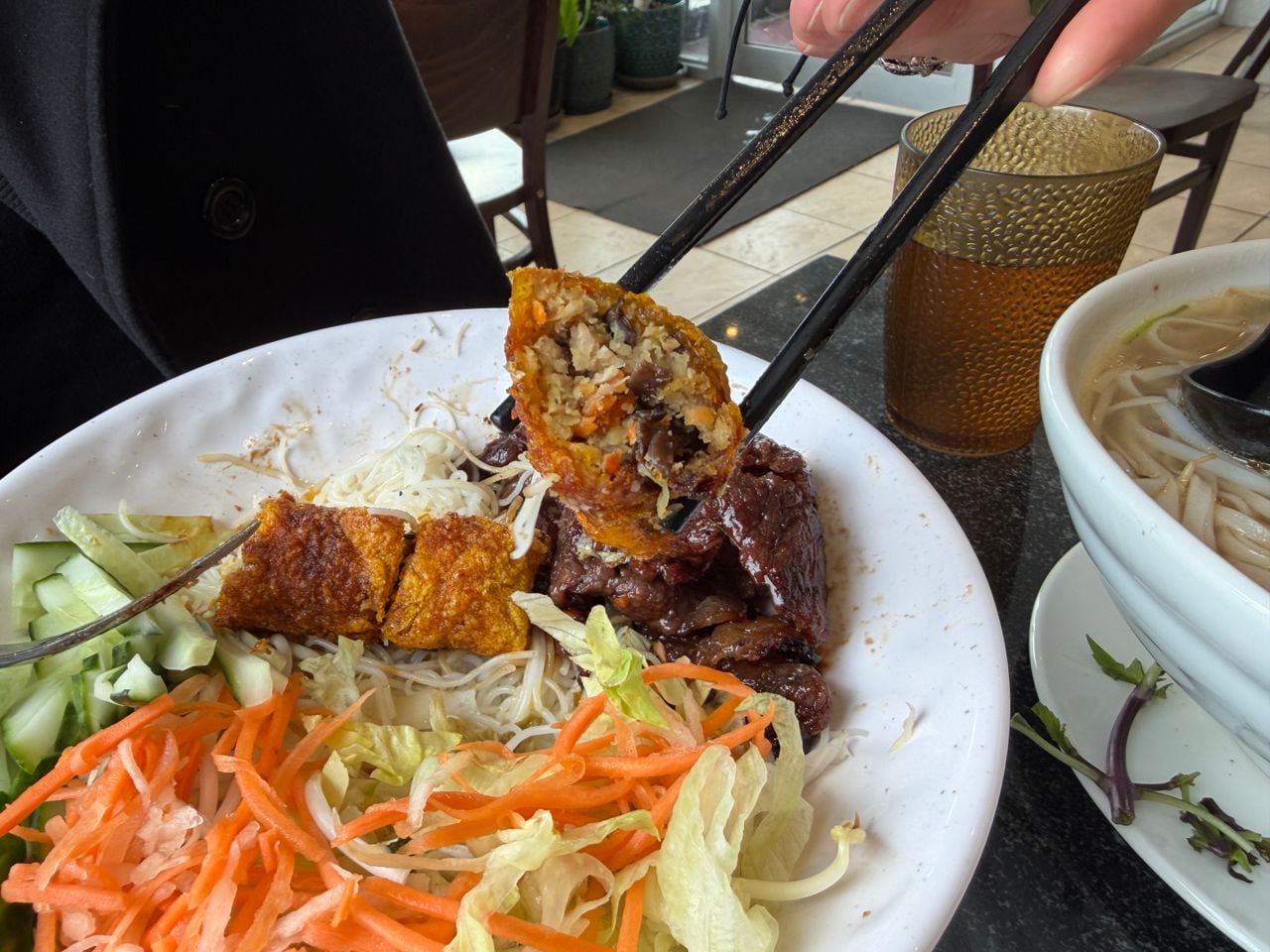A closeup of a piece of spring roll between chopsticks