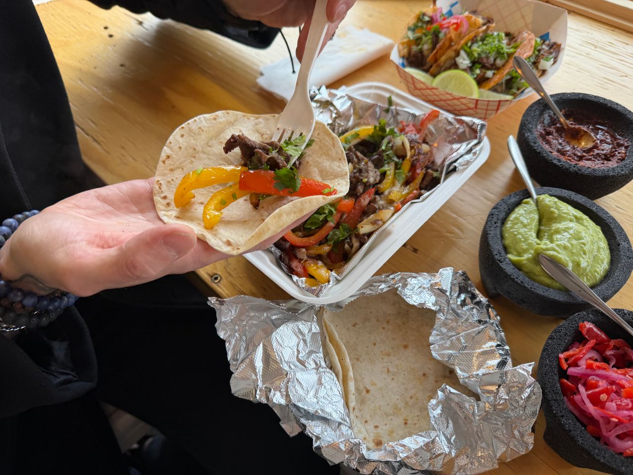 A person makes a small taco using a tortilla and beef