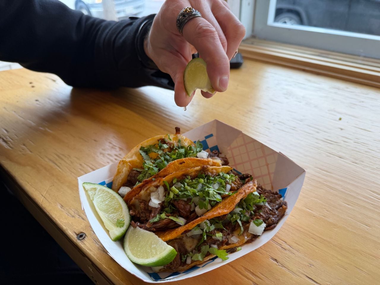 A person squeezes a lime wedge over an order of three tacos