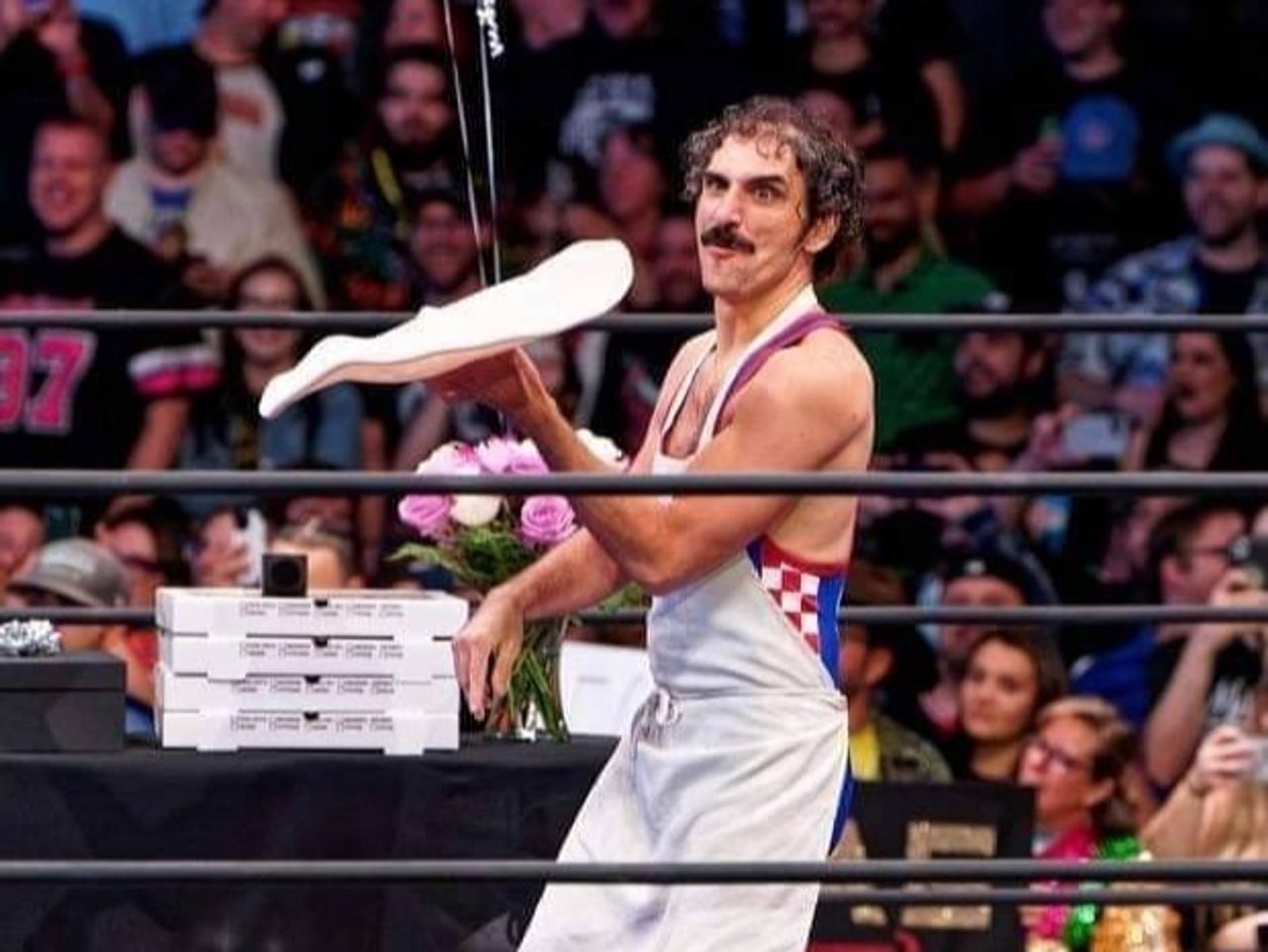 Luigi Primo twirls pizza dough while standing in a wrestling ring.