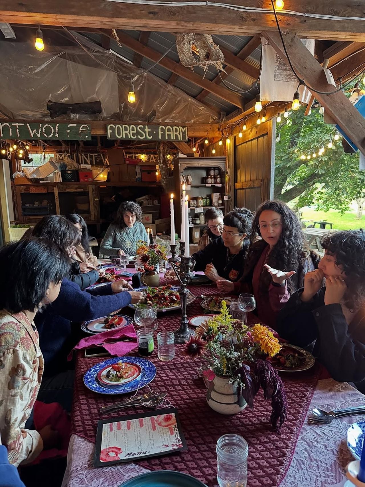 A group of people gather at a table inside a barn