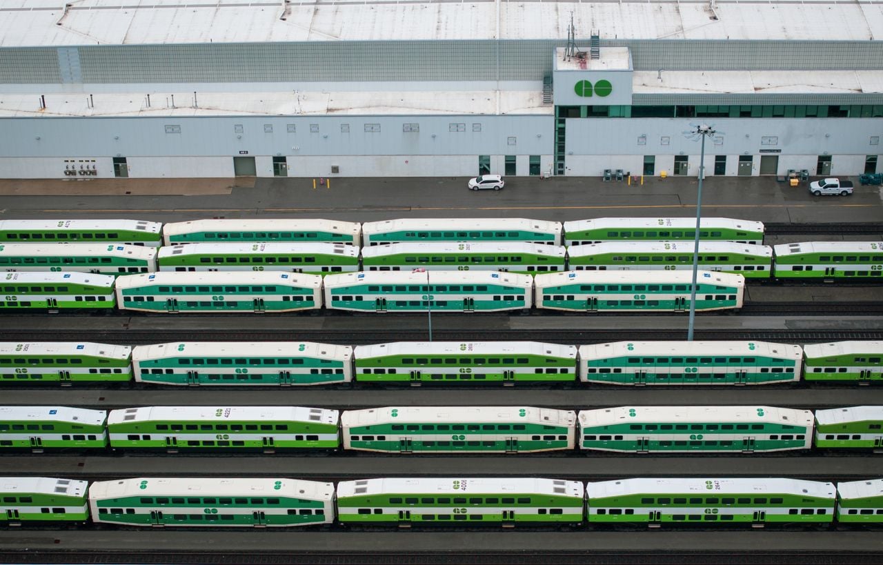 Lines of GO trains wait on tracks outside of a large station.