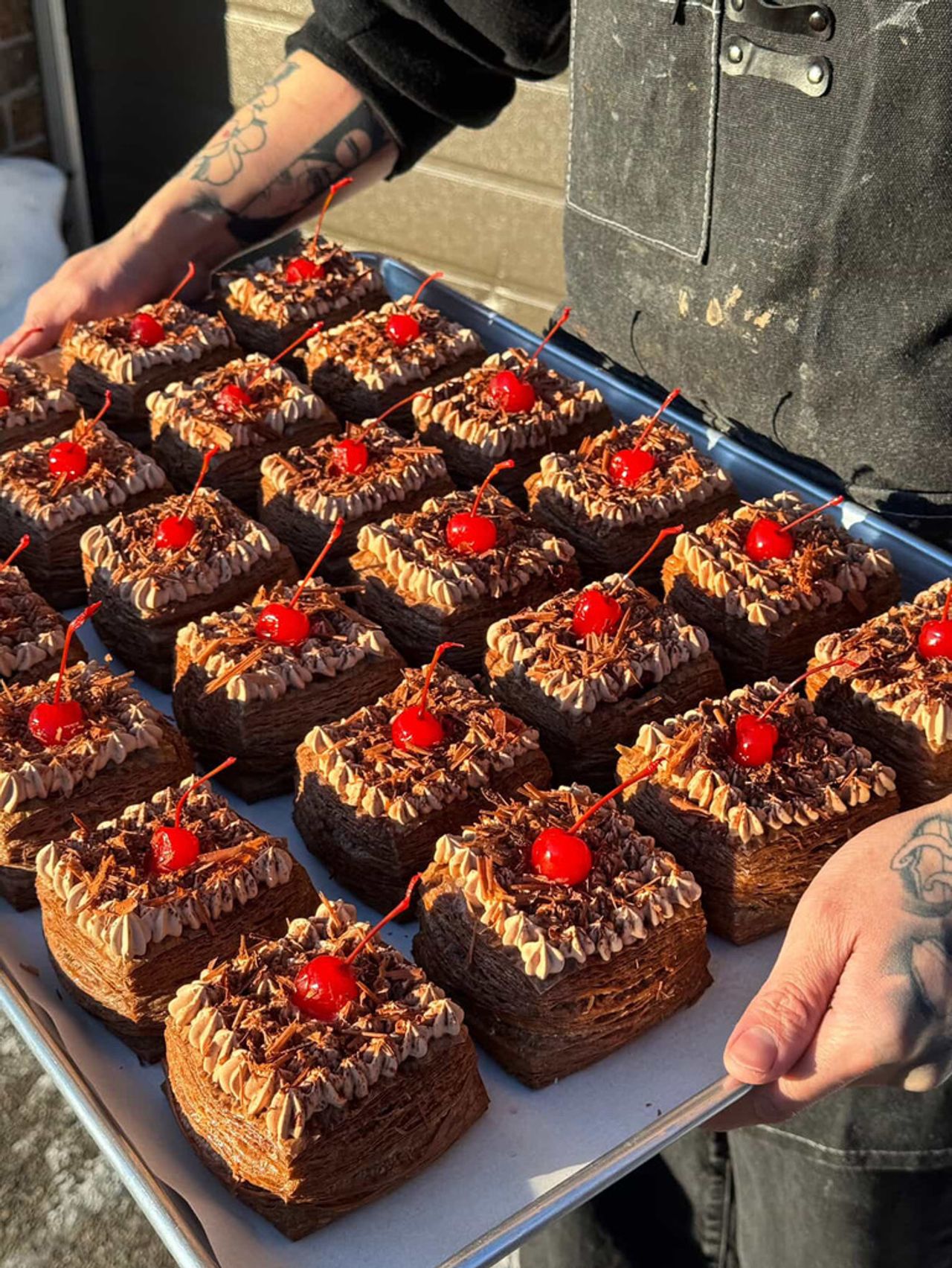 A person holds a tray of pastries topped with icing and cherries