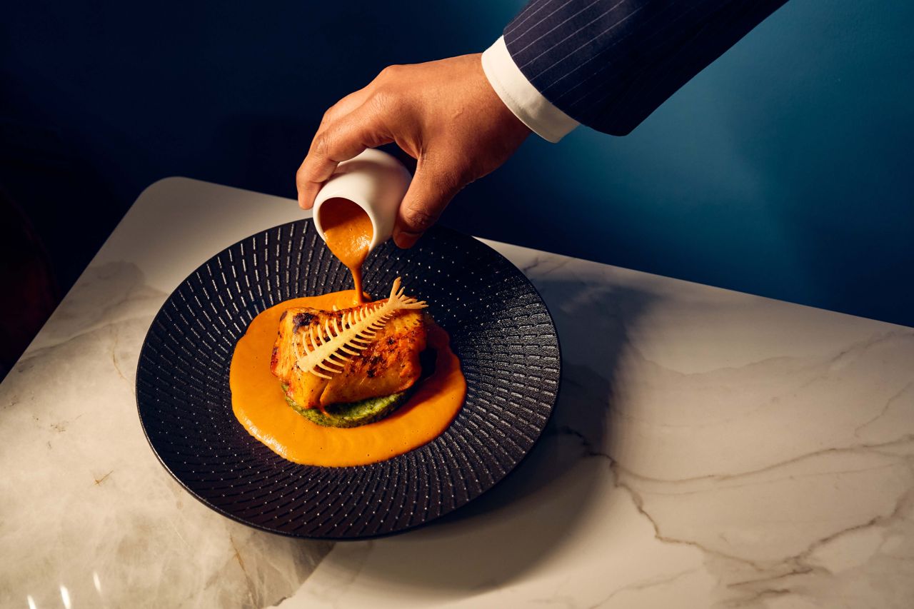 A server pours sauce over a cod dish at Aangan