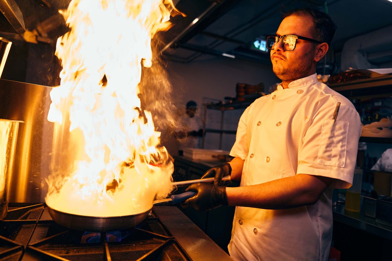 A chef holds a pan that's in flames over a stove