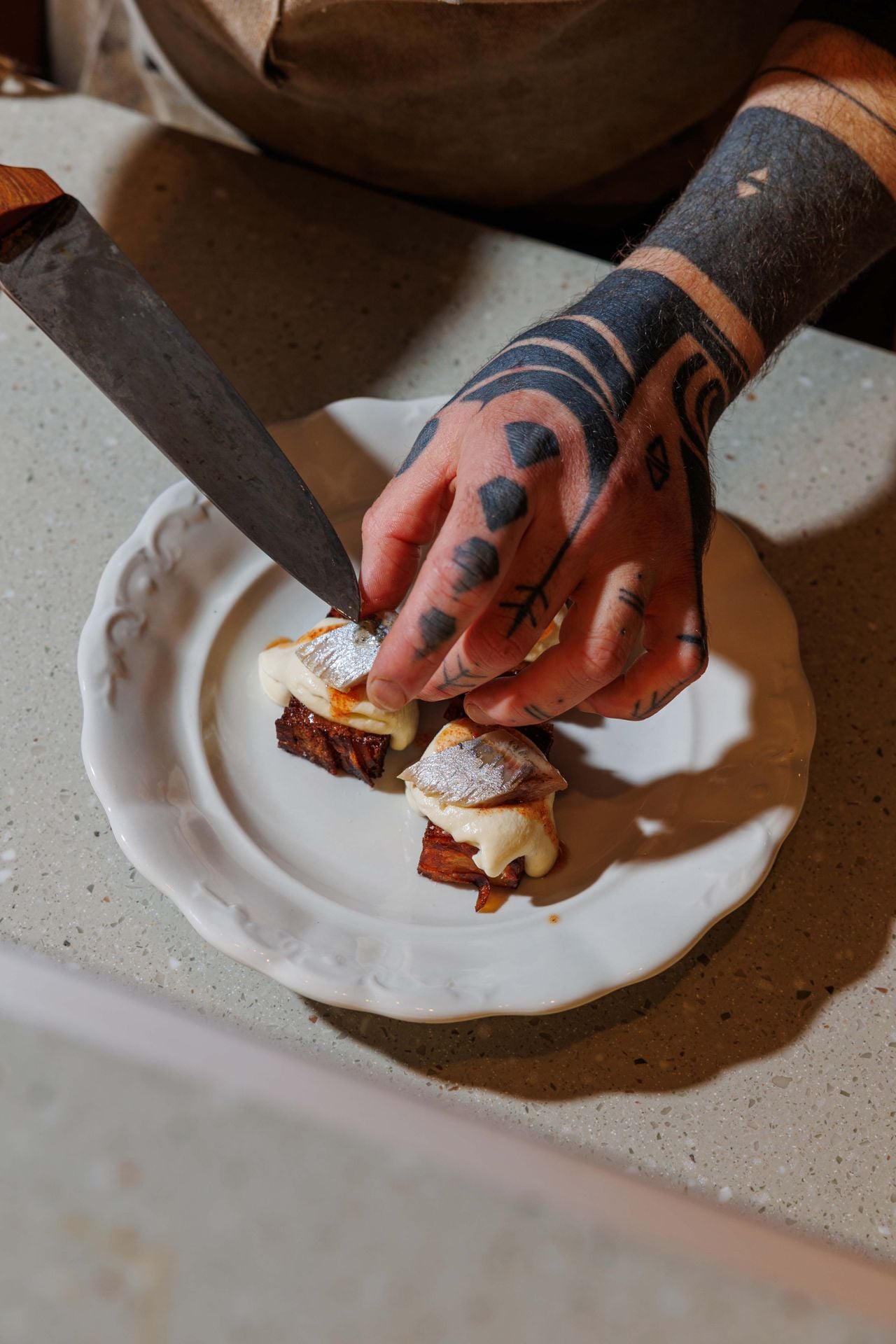 A chef uses a knife to place a sardine on a dish