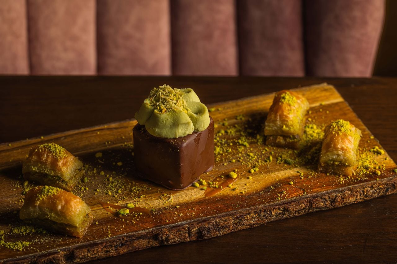A glossy cube of chocolate mousse sits at the centre of this plate, topped with rosettes of pistachio cream, flanked by a tumble of kataifi and finished with a dusting of ground pistachio
