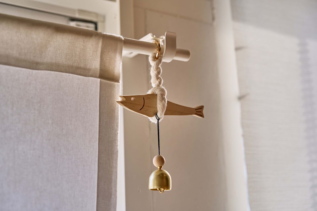 A wooden fish attached to a bell hangs from a curtain rod