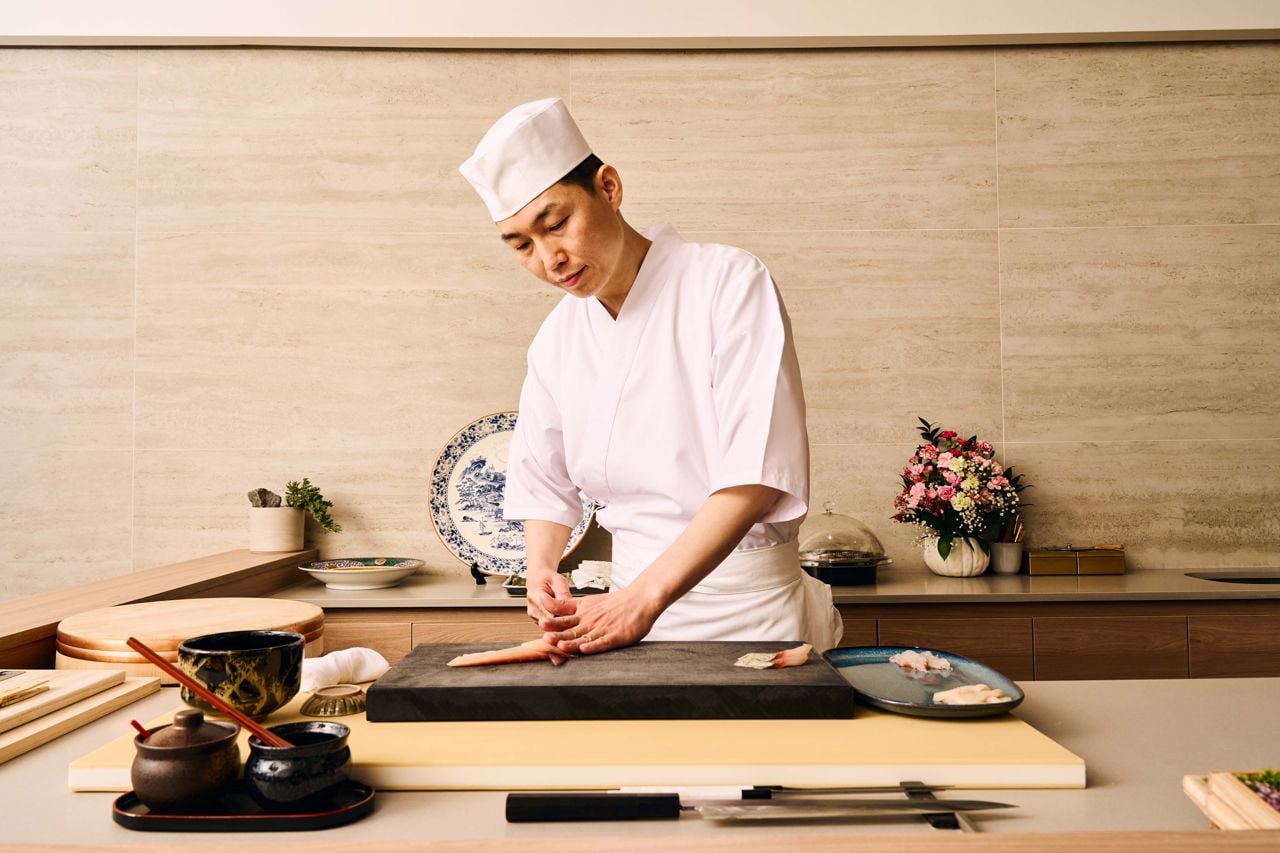 A sushi chef slices a piece of fish behind the counter of an omakase restaurant