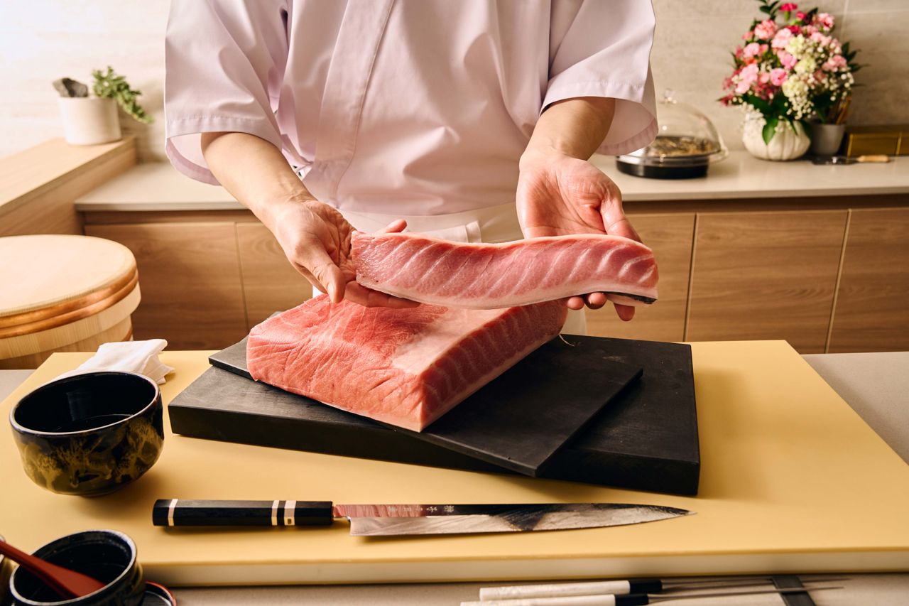 A sushi chef holds up a thick slab of tuna