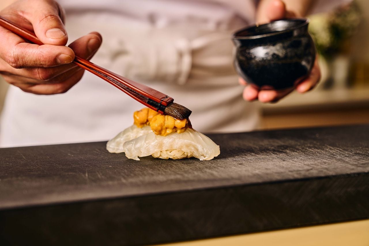A sushi chef paints a piece of sea urchin with soy sauce
