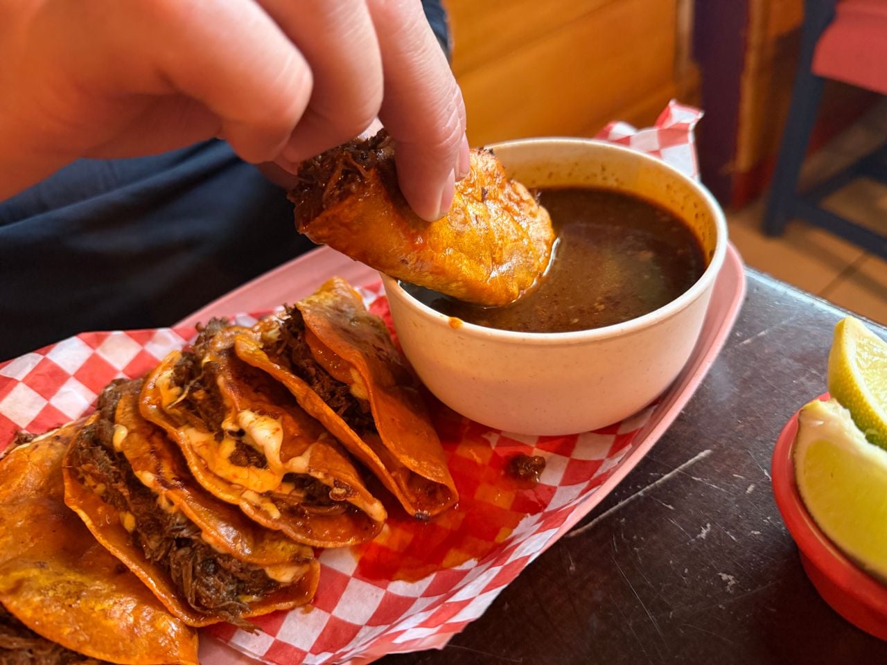 A person dips a birria taco into a bowl of consome
