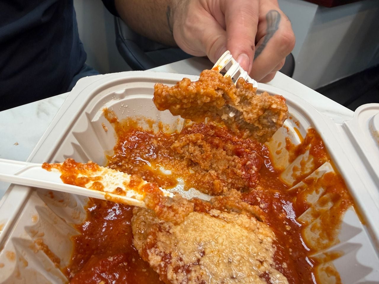 A person uses a fork and knife to eat a saucy veal cutlet