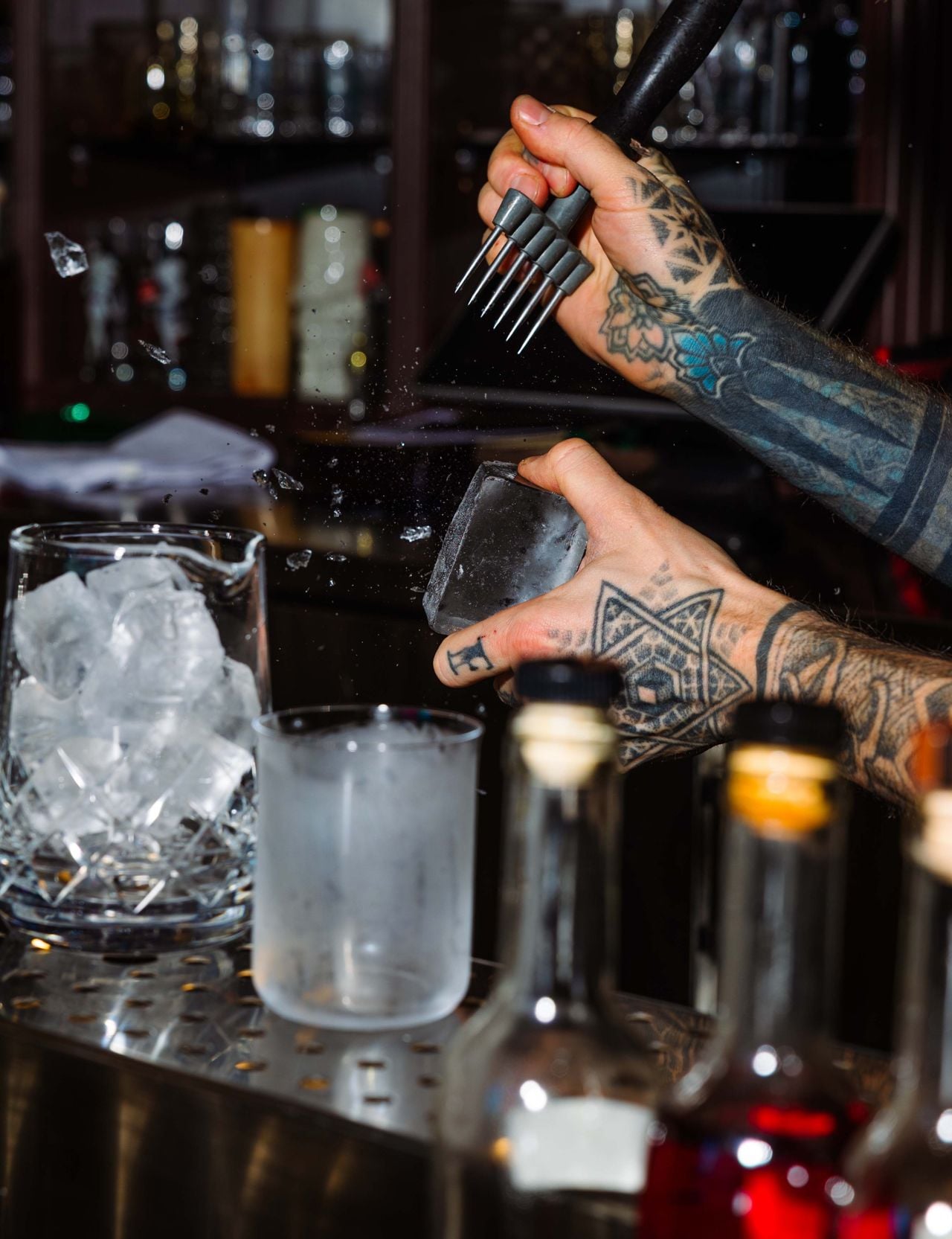 A bartender chips a large ice cube