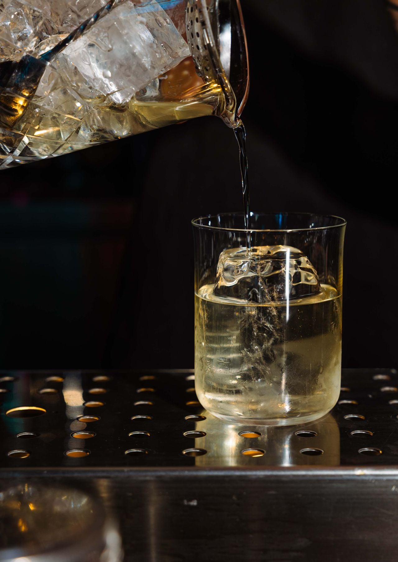 A cocktail is poured from a mixing glass into a glass