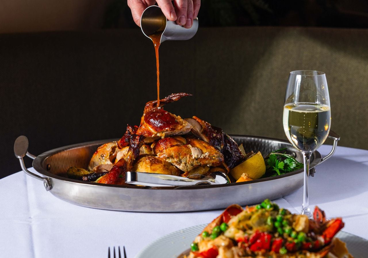 A server pours gravy over a whole roasted chicken