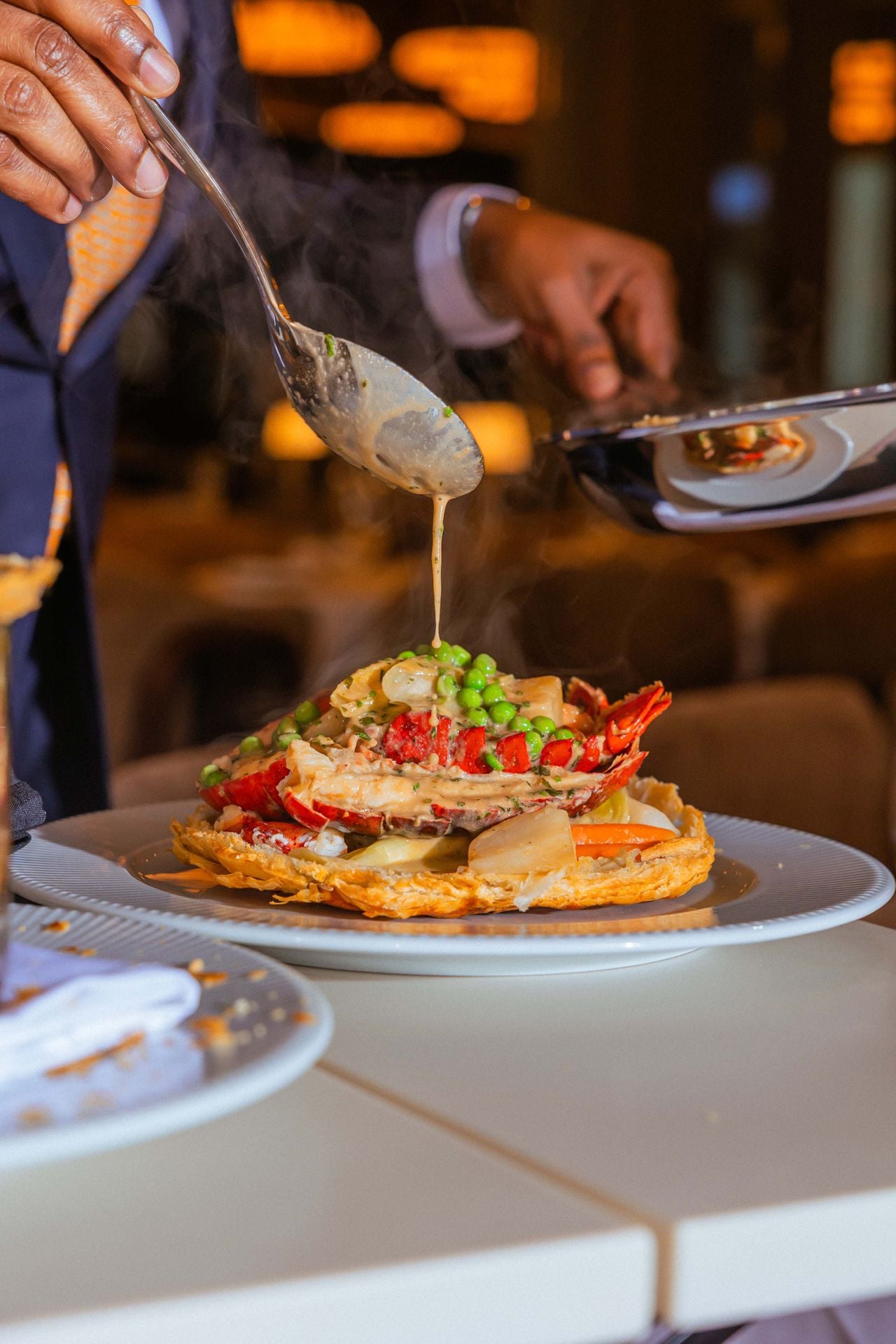 A server pours sauce over a serving of lobster pot pie