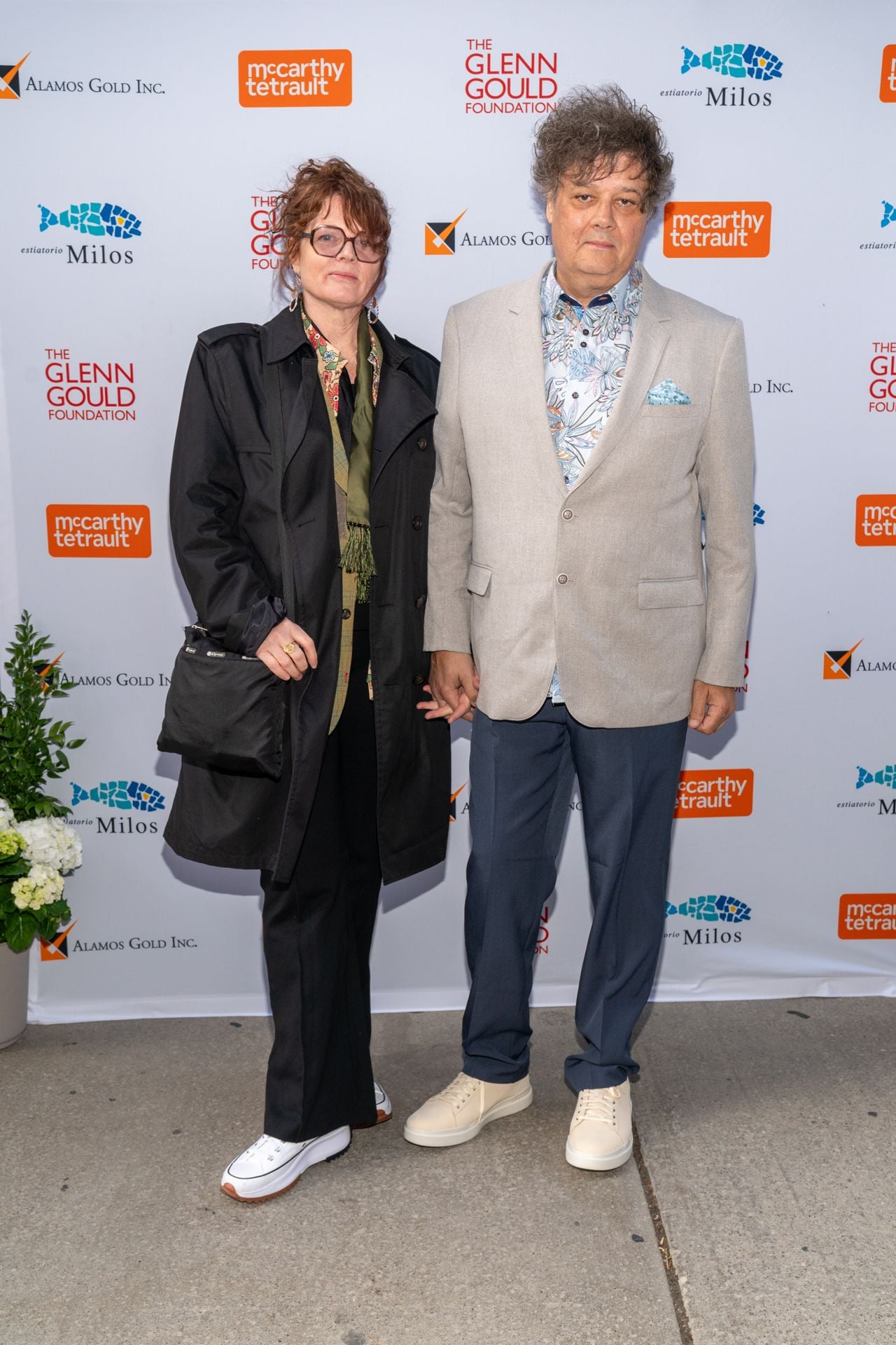 Woman in funky glasses wearing Converse shoes next to a man wearing a grey suit jacket