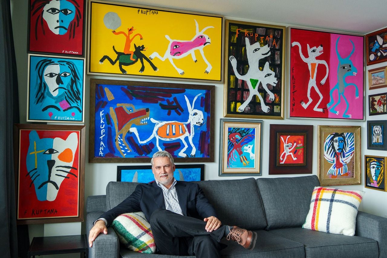 Man sitting on a couch in front of a gallery wall of paintings
