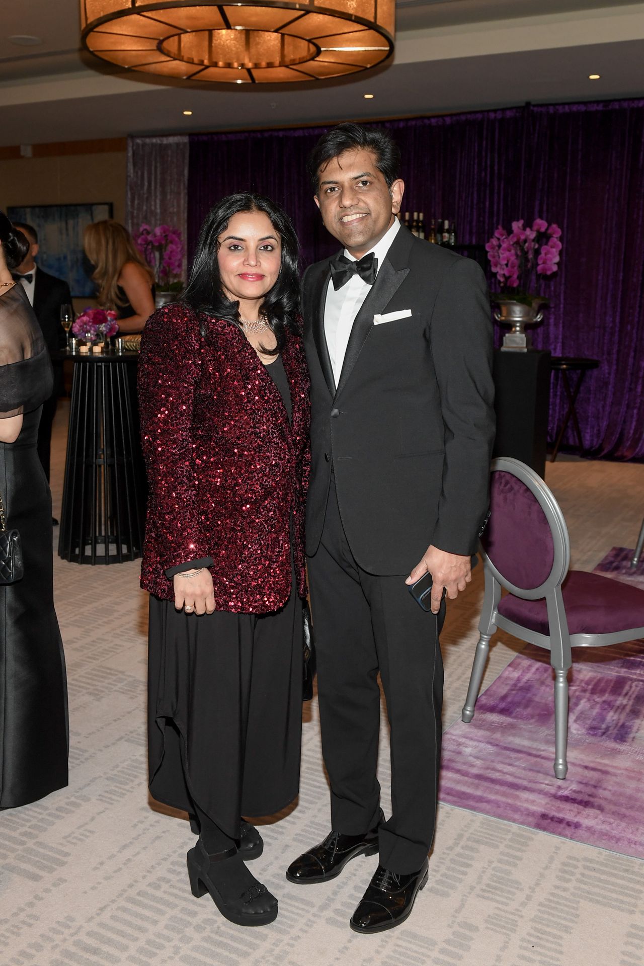 Woman in red sequin jacket and black skirt next to a man in a black suit