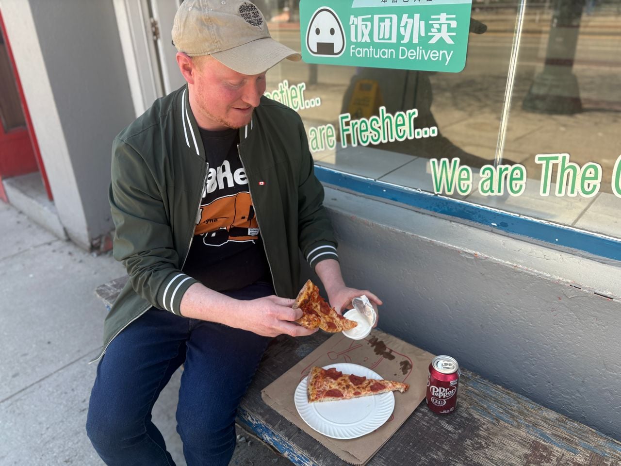 Chef Adam Ryan sits on a bench outside of Cora's Pizza with a slice of pepperoni pizza