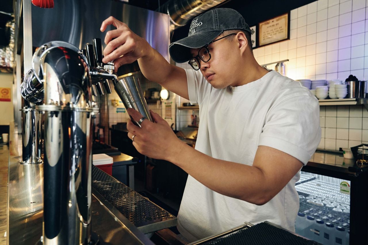 A bartender pours makgeolli from a tap into a cup