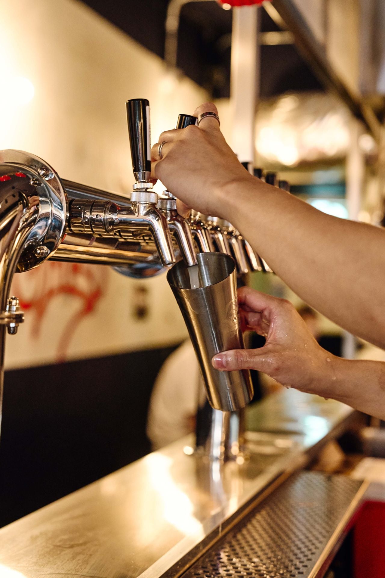 A bartender pours makgeolli from a tap into a metal cup