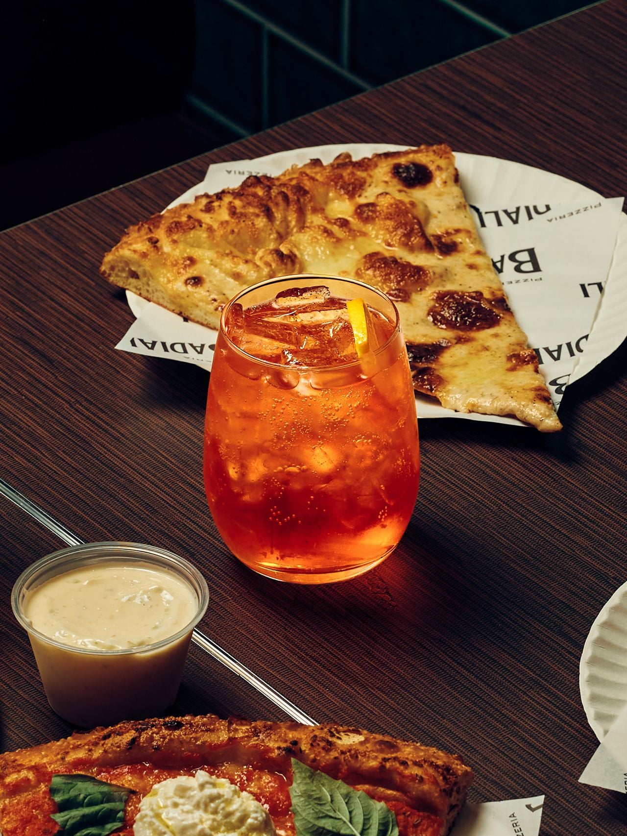 An Aperol Spritz next to a slice of pizza