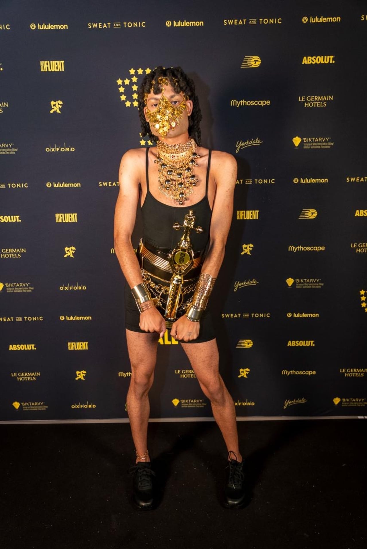 A performer in a black outfit with gold accessories, including a gold beaded face covering