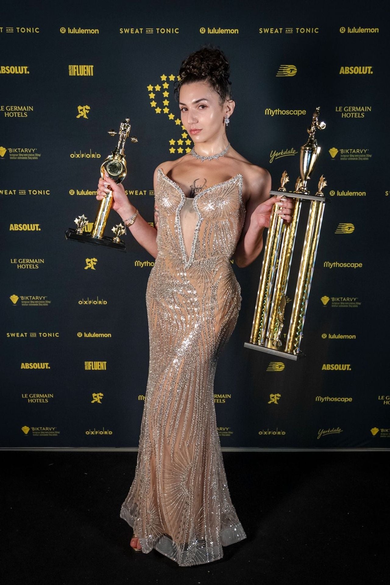 A performer in a sheer gown holding two trophies