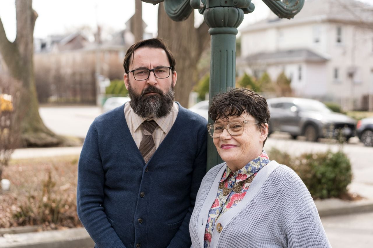 A man and a woman in cardigans and glasses on the street