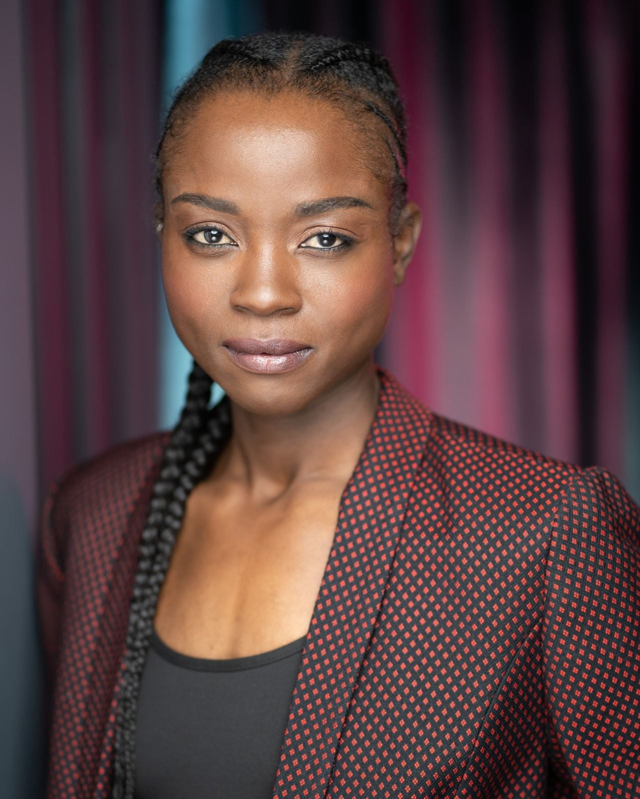 A portrait of a woman with braids wearing a maroon blazer