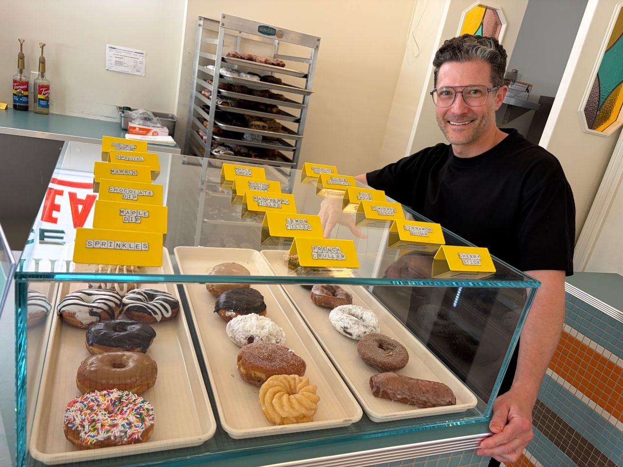 Adam Minster stands next to the display of doughnuts at Better Days Coffee and Donuts