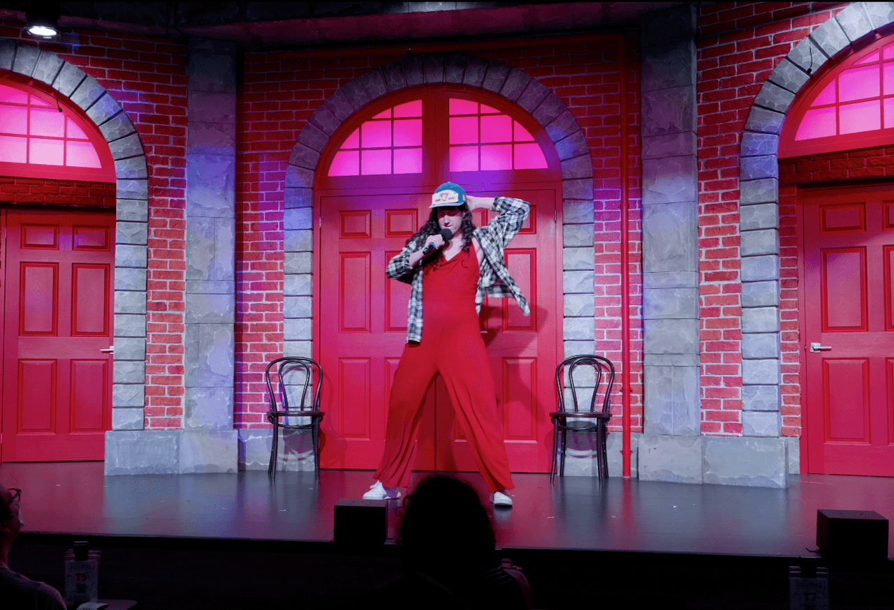 A woman on stage in a red jumpsuit wearing a TTC hat
