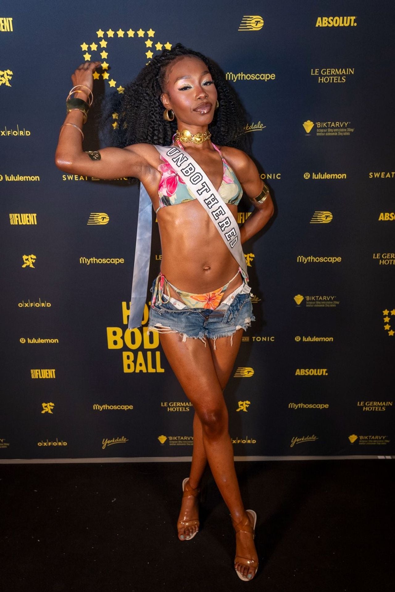 A performer in jean shorts, a bikini and a sash that reads "Unbothered"