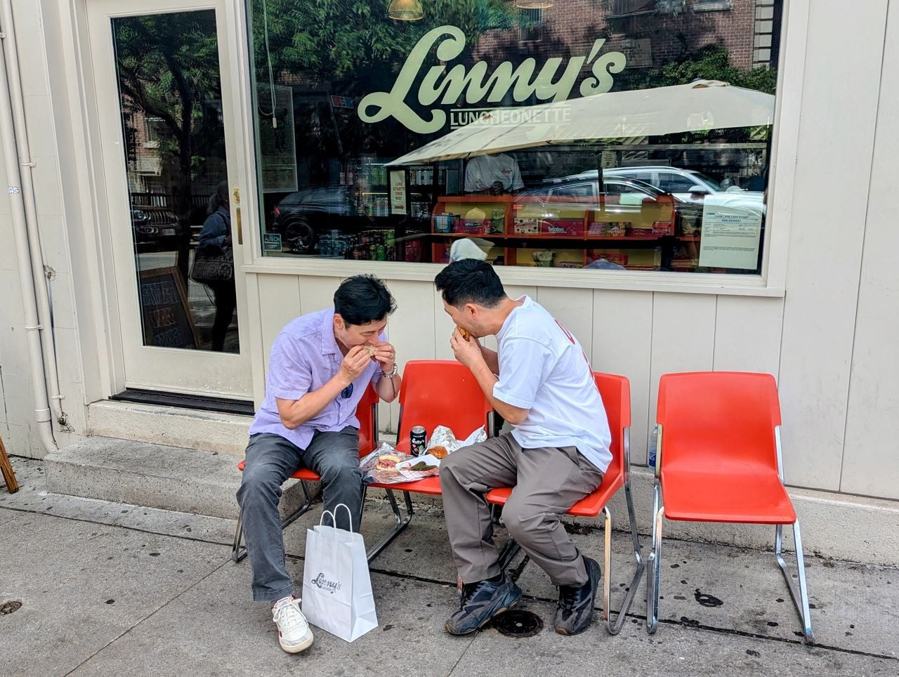 Chefs Ed Bang and Jeff Kang eat sandwiches outside Linny's Luncheonette