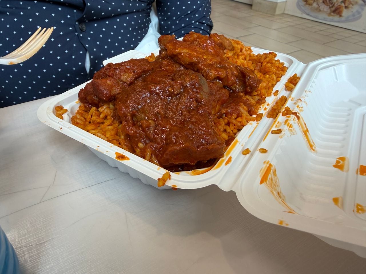 A container of chicken stew with jollof rice