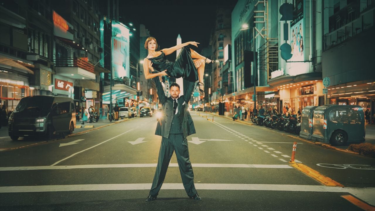 A man in a suit holding a woman in a dress above his head on a city street