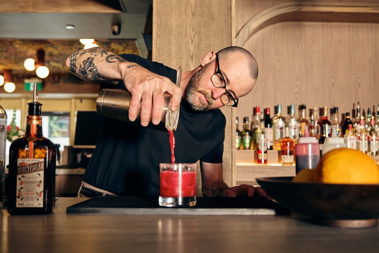 A bartender pours a drink from a shaker into a glass