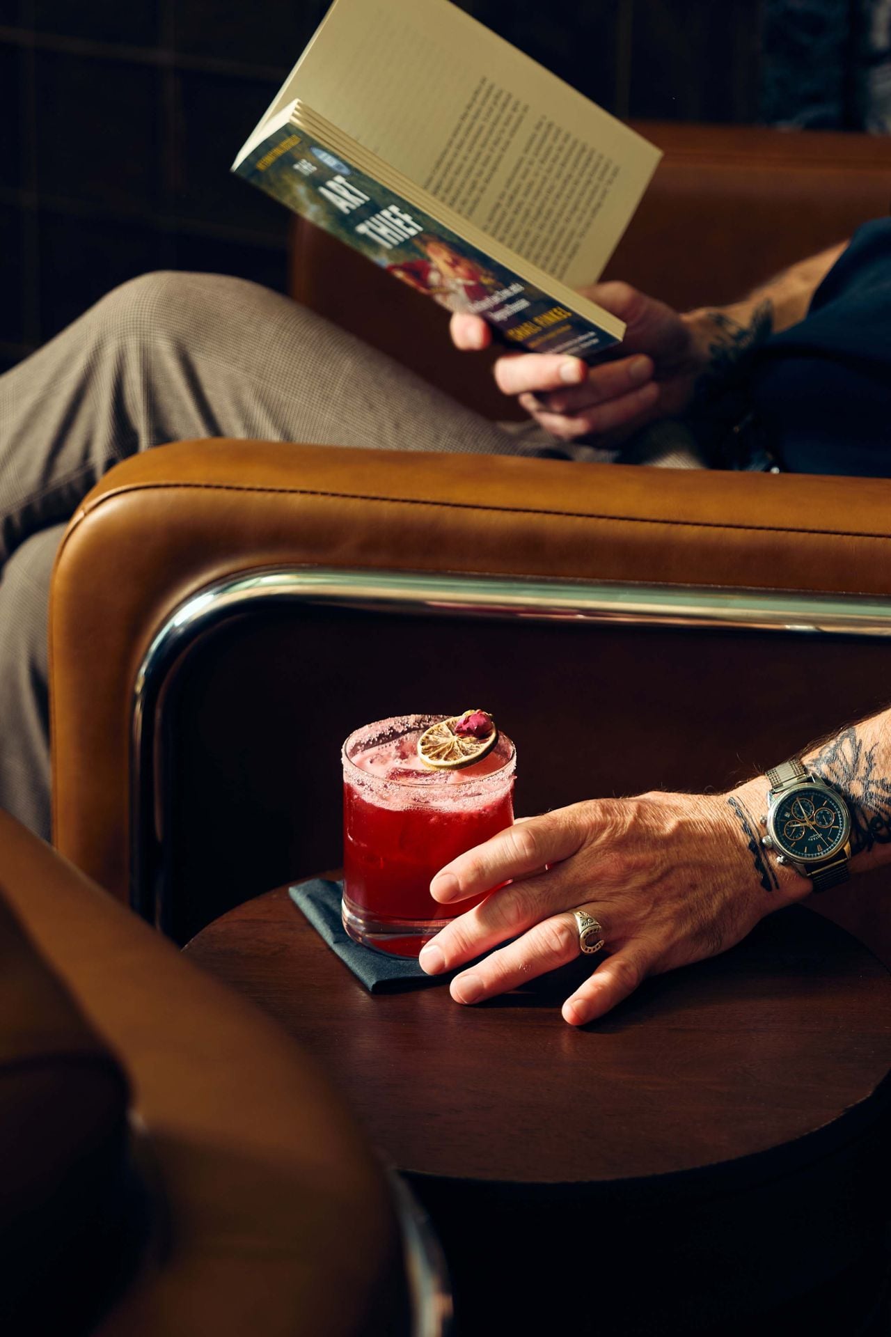 A person sitting in a chair reading a book reaches for a cocktail