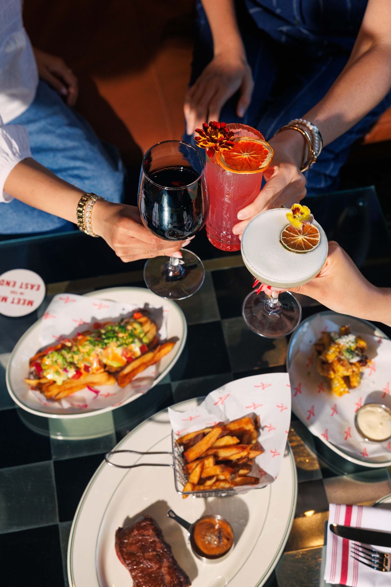 People clink cocktails over a table set with dishes