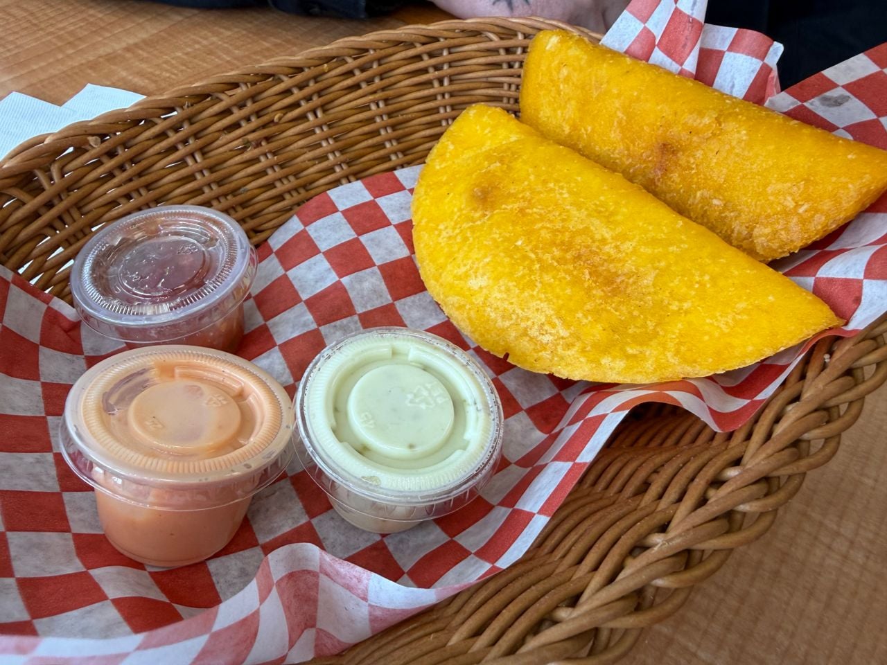A basket with two empanadas and three containers of sauce