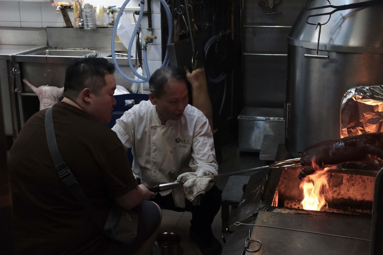 A cook at Moon Bay in Hong Kong roasts a suckling pig while chef Eva Chin looks on